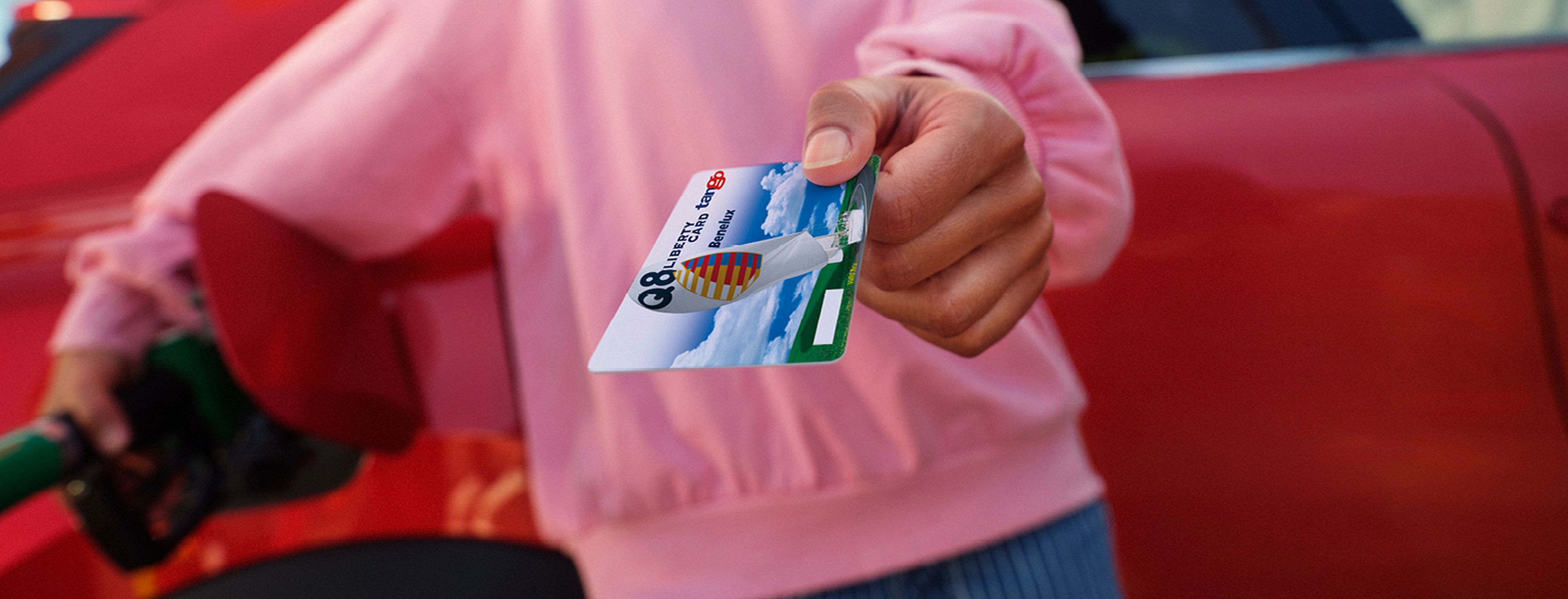 Une main tient une carte de carburant Q8 Liberty avec des voitures en arrière-plan