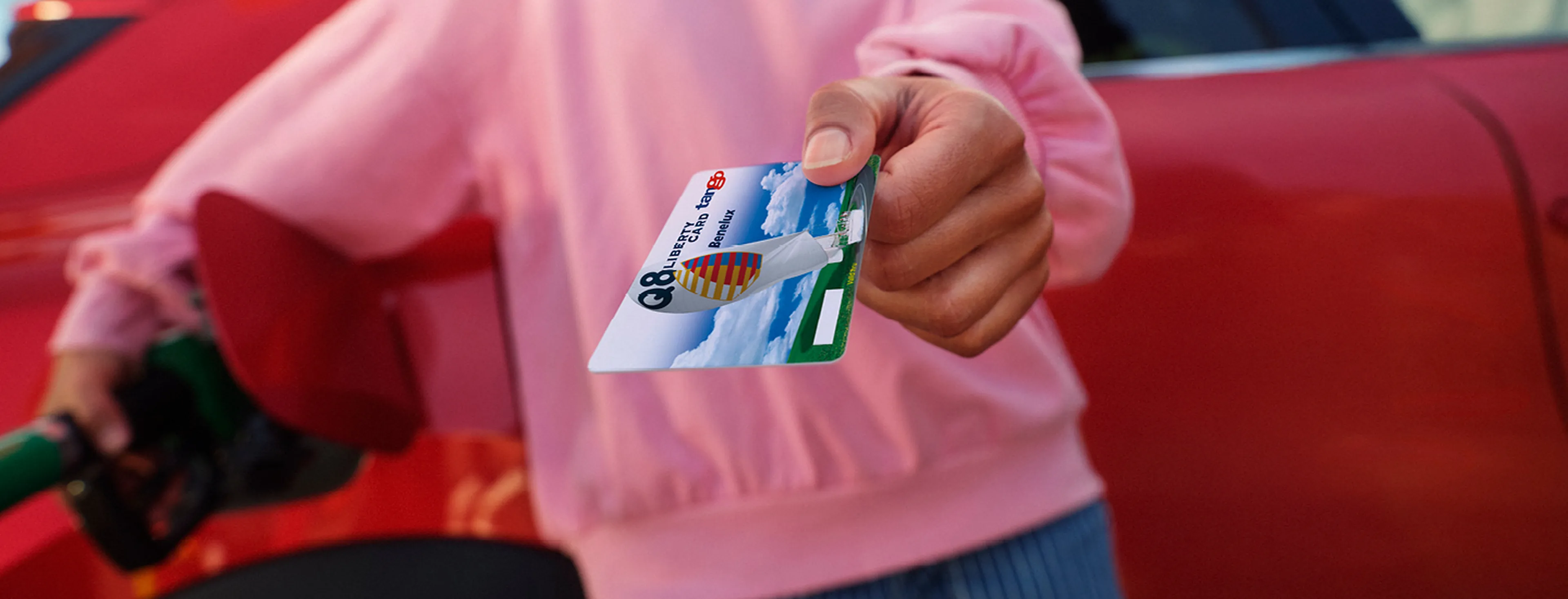 Een hand houdt een Q8 liberty card vast tegen een achtergrond van een drukke stadssnelweg met fileverkeer in de schemering.