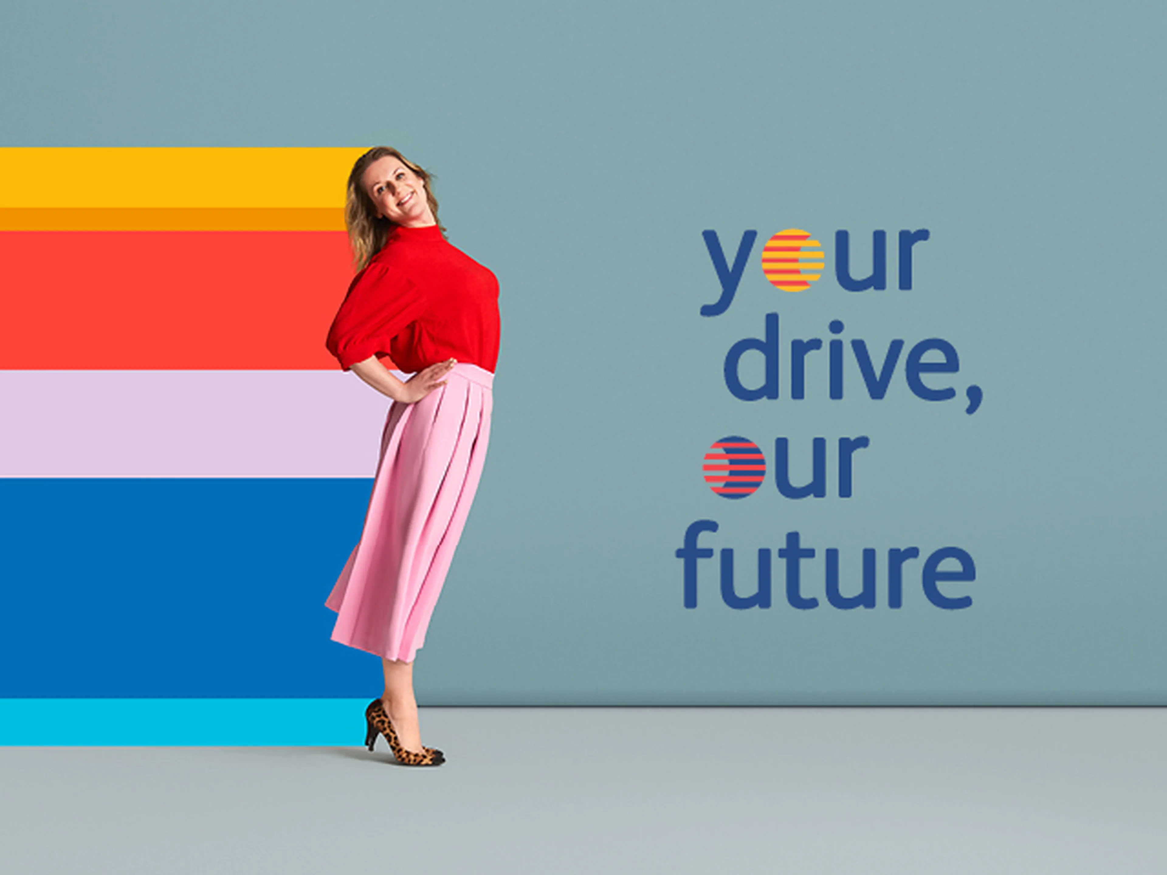Een vrouw poseert vrolijk met een lichte buiging naar achteren tegen een effen blauwe achtergrond. Ze draagt een rode top, een roze geplooide rok tot halverwege de kuit en luipaardprint-hakken.
