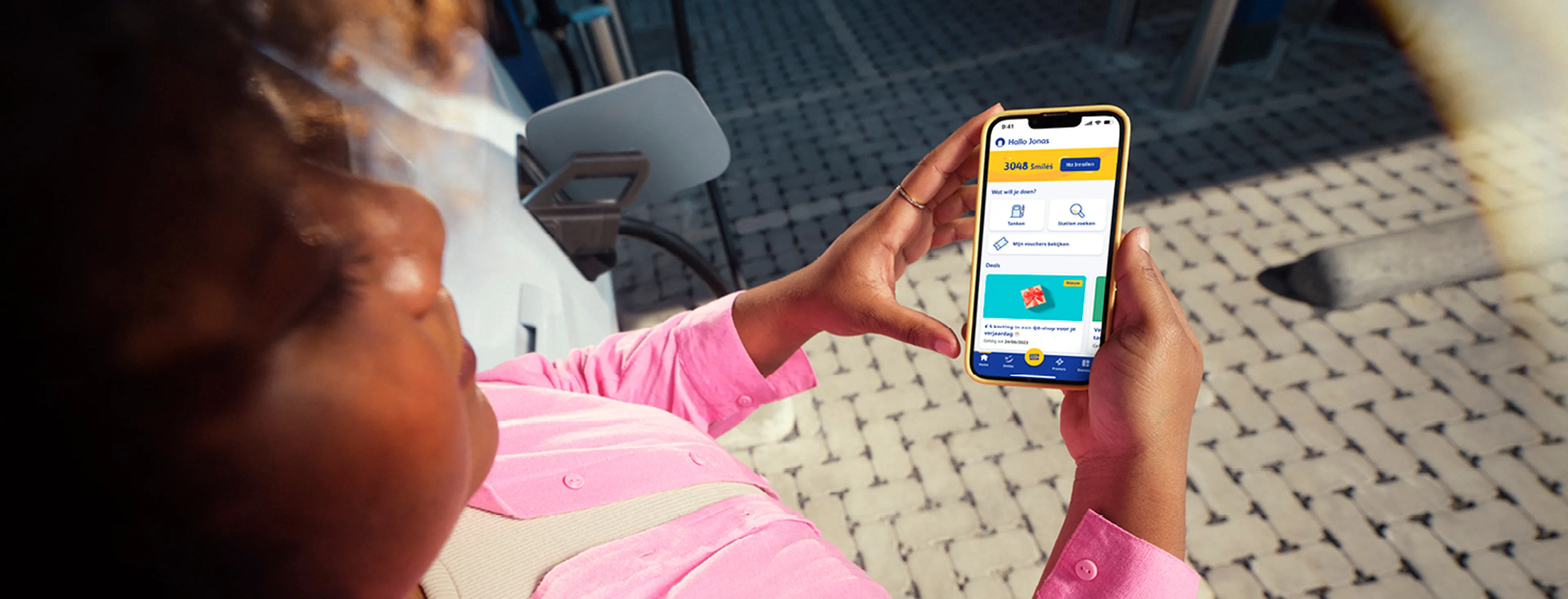 Vrouw bekijkt de Q8 app op haar telefoon bij een Q8 tankstation.