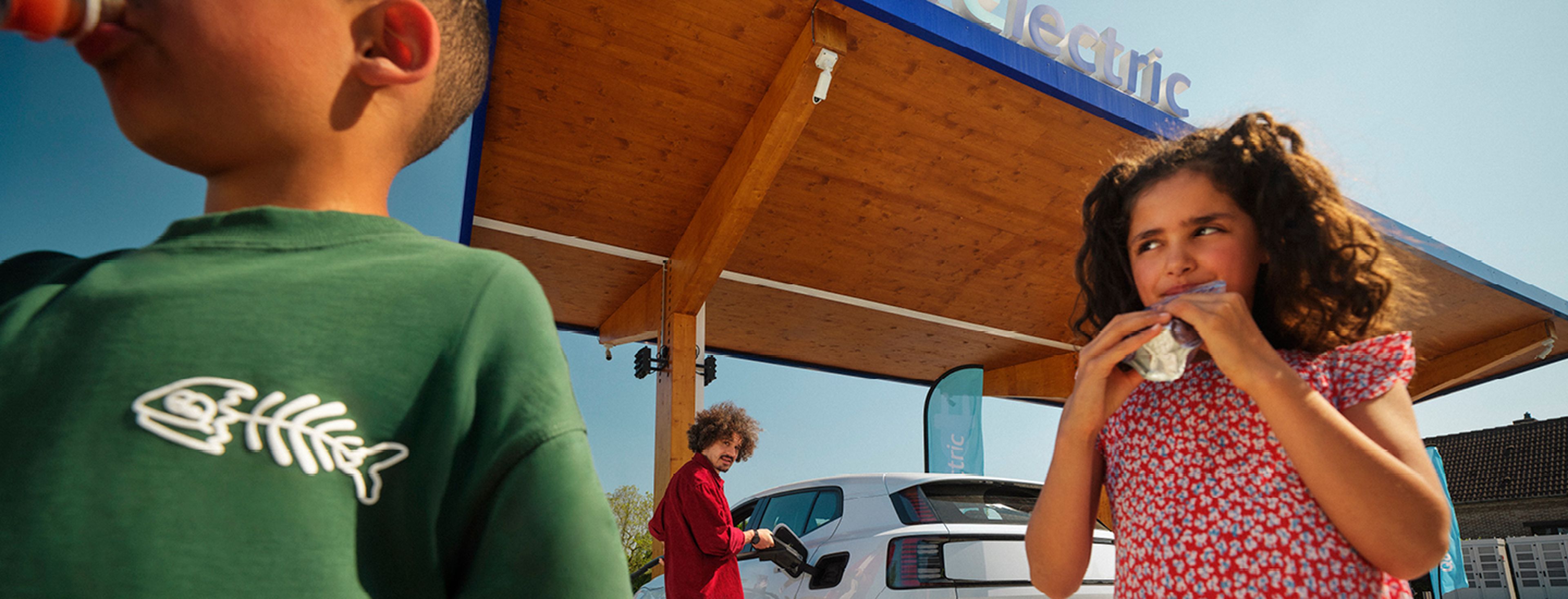 Kinderen drinken terwijl een man een elektrische auto laadt bij een Q8 Electric station