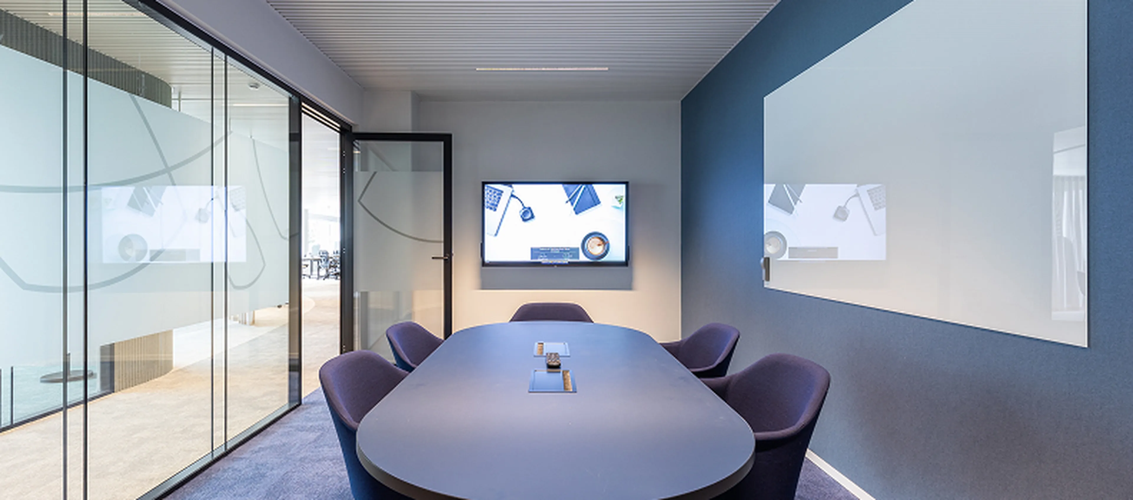 Modern meeting room at the Q8 headquarters in Antwerp. Glass walls, oval table, purple chairs, and a large whiteboard.