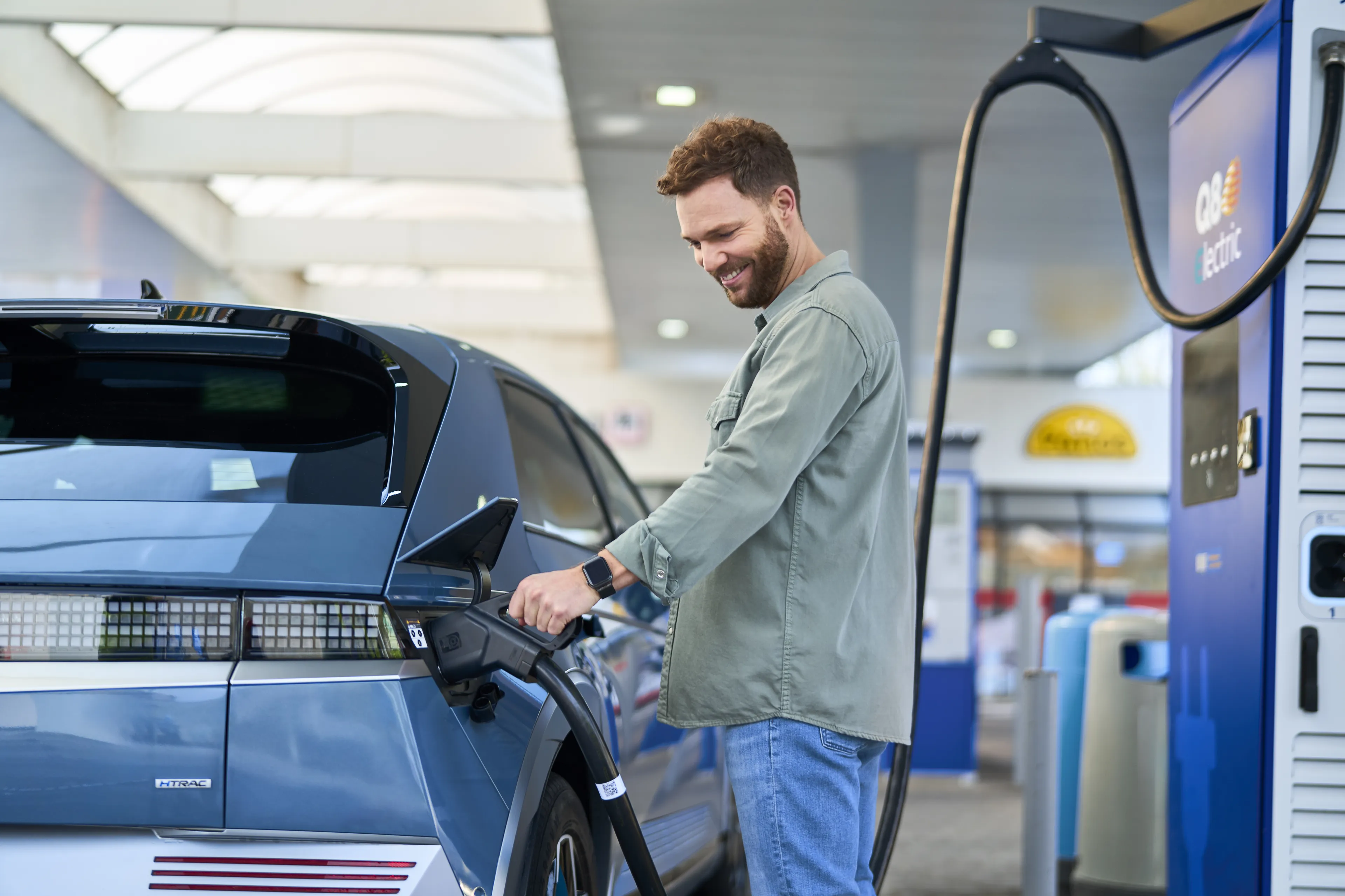 man steekt lader in auto bij Q8 electric