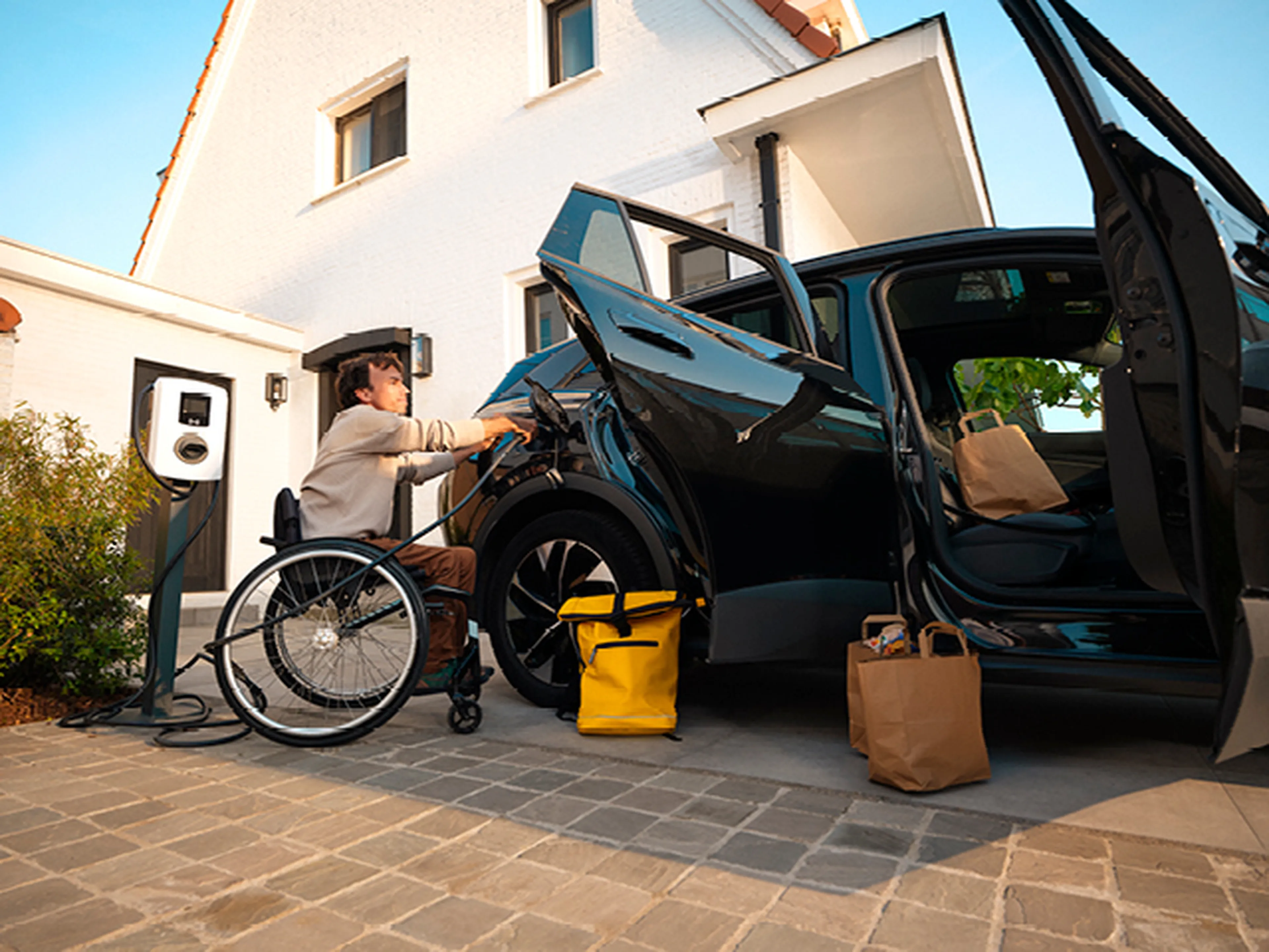 Man in rolstoel laadt elektrische auto op met een thuislader van Q8 electric.