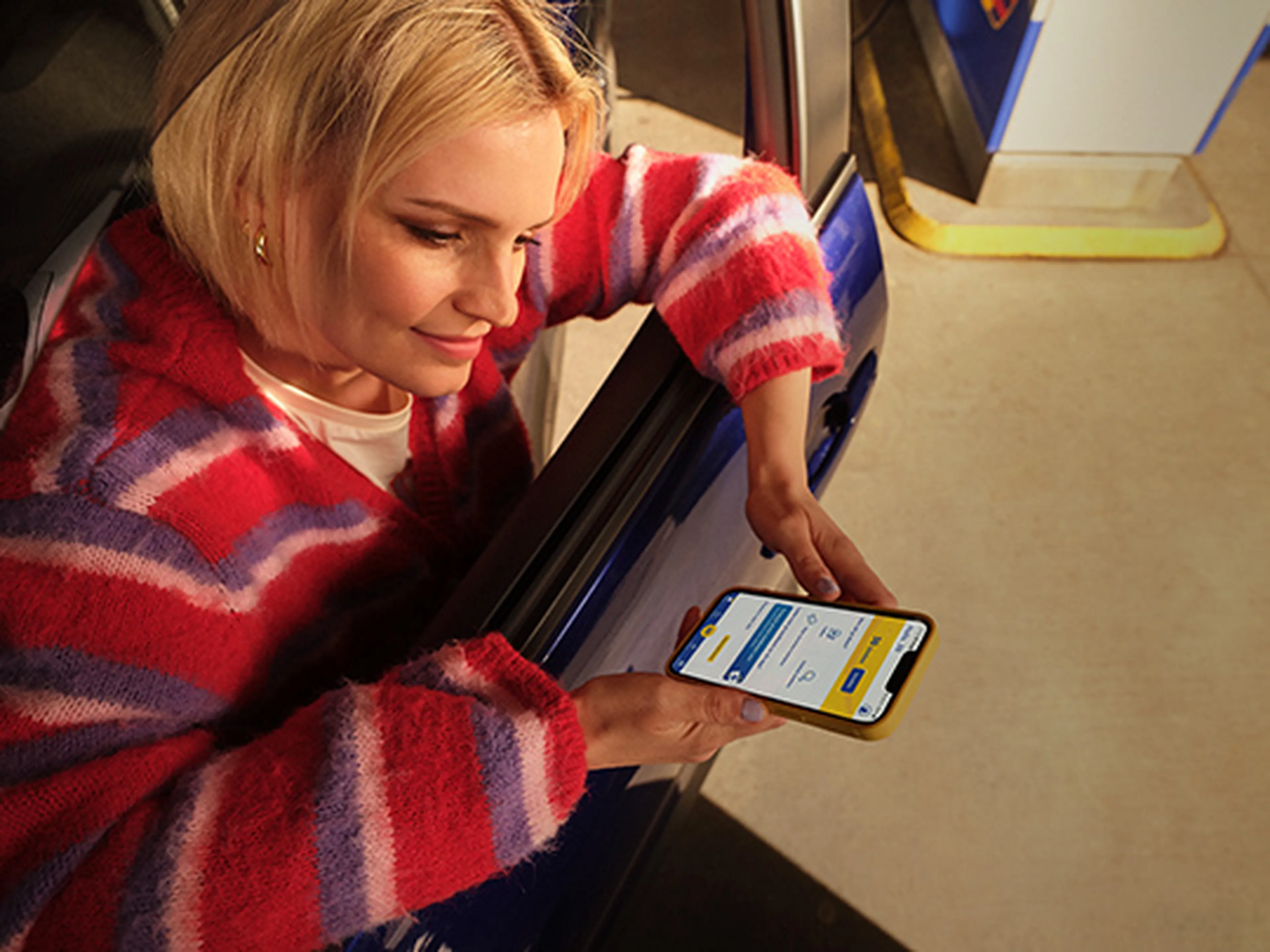 Femme assise dans sa voiture utilise l’app Q8 sur son smartphone dans une station Q8