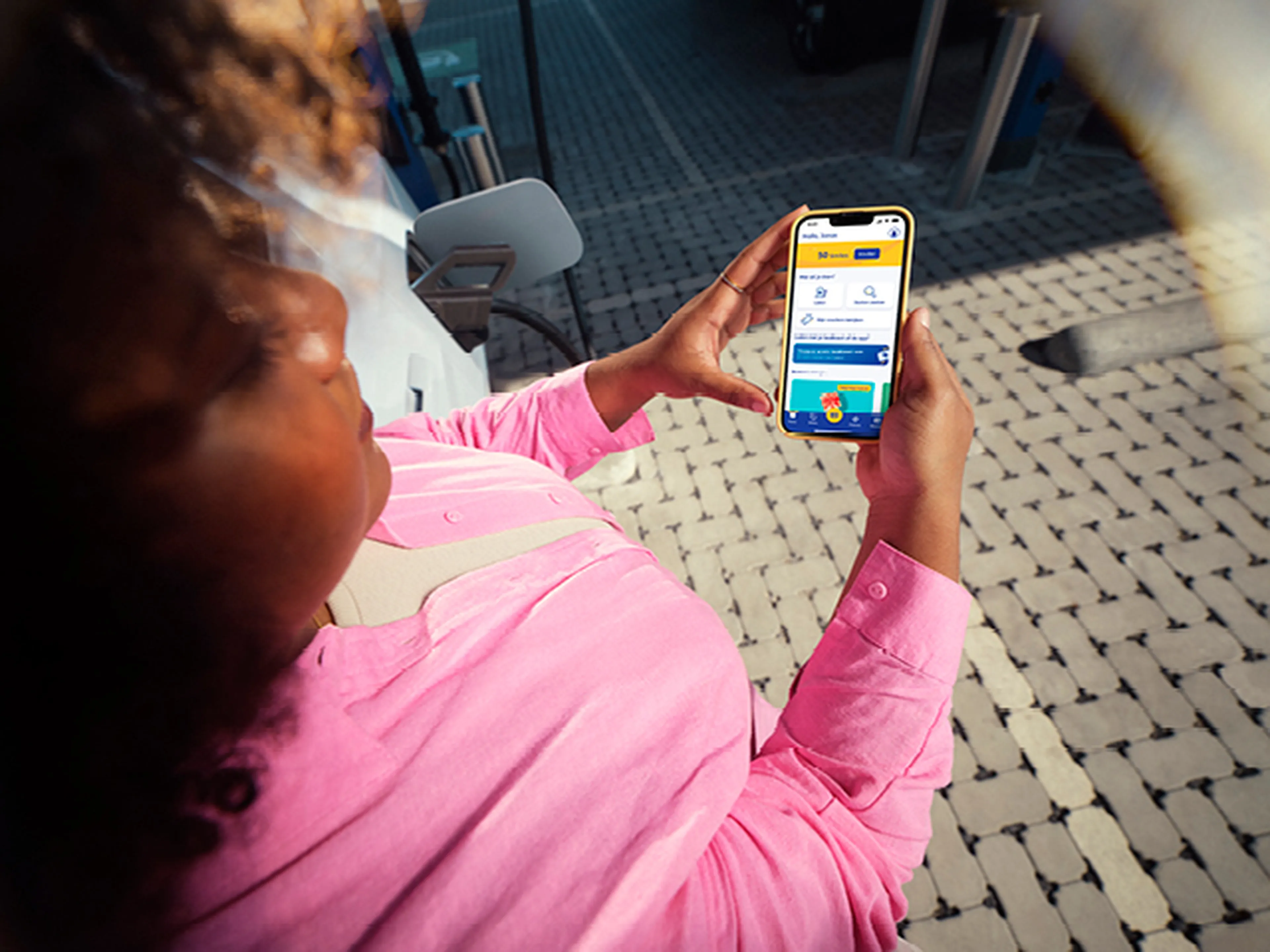 Femme regarde son téléphone à écran près d'une station de recharge Q8.