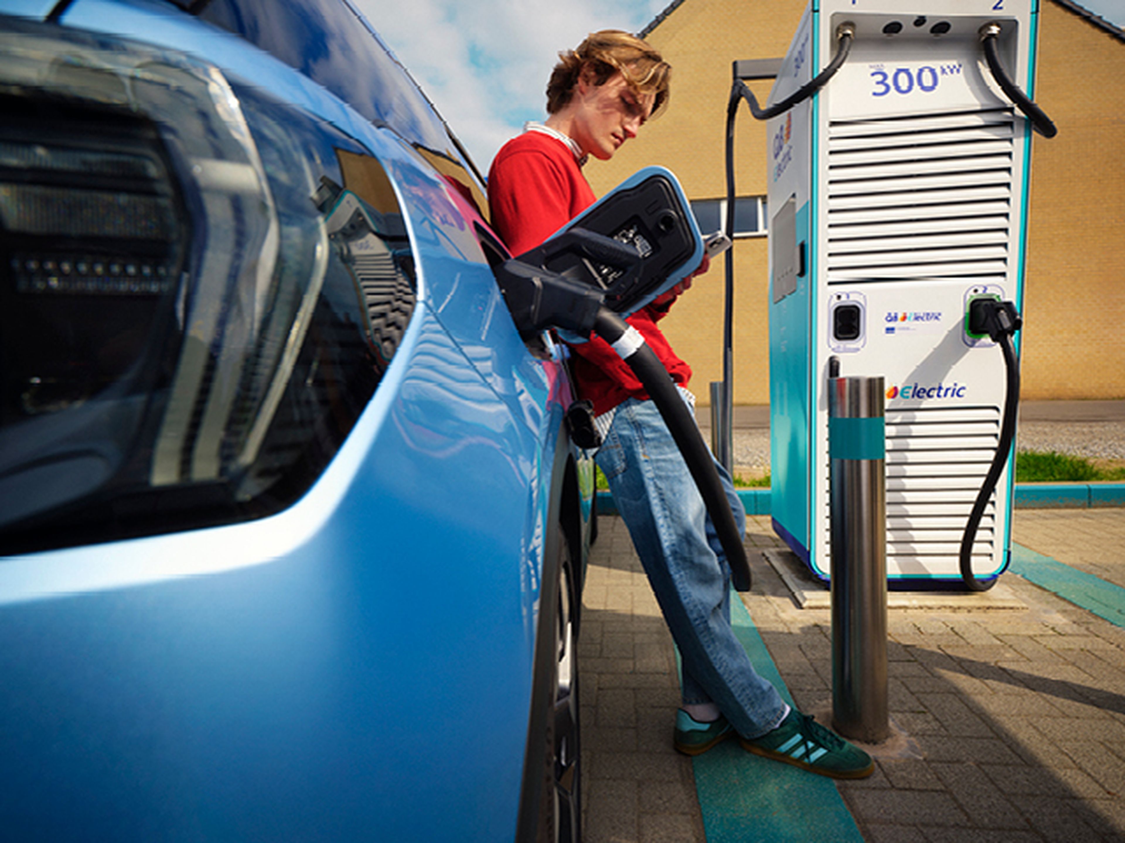 Man met gsm bij Q8 electric terwijl hij laadt