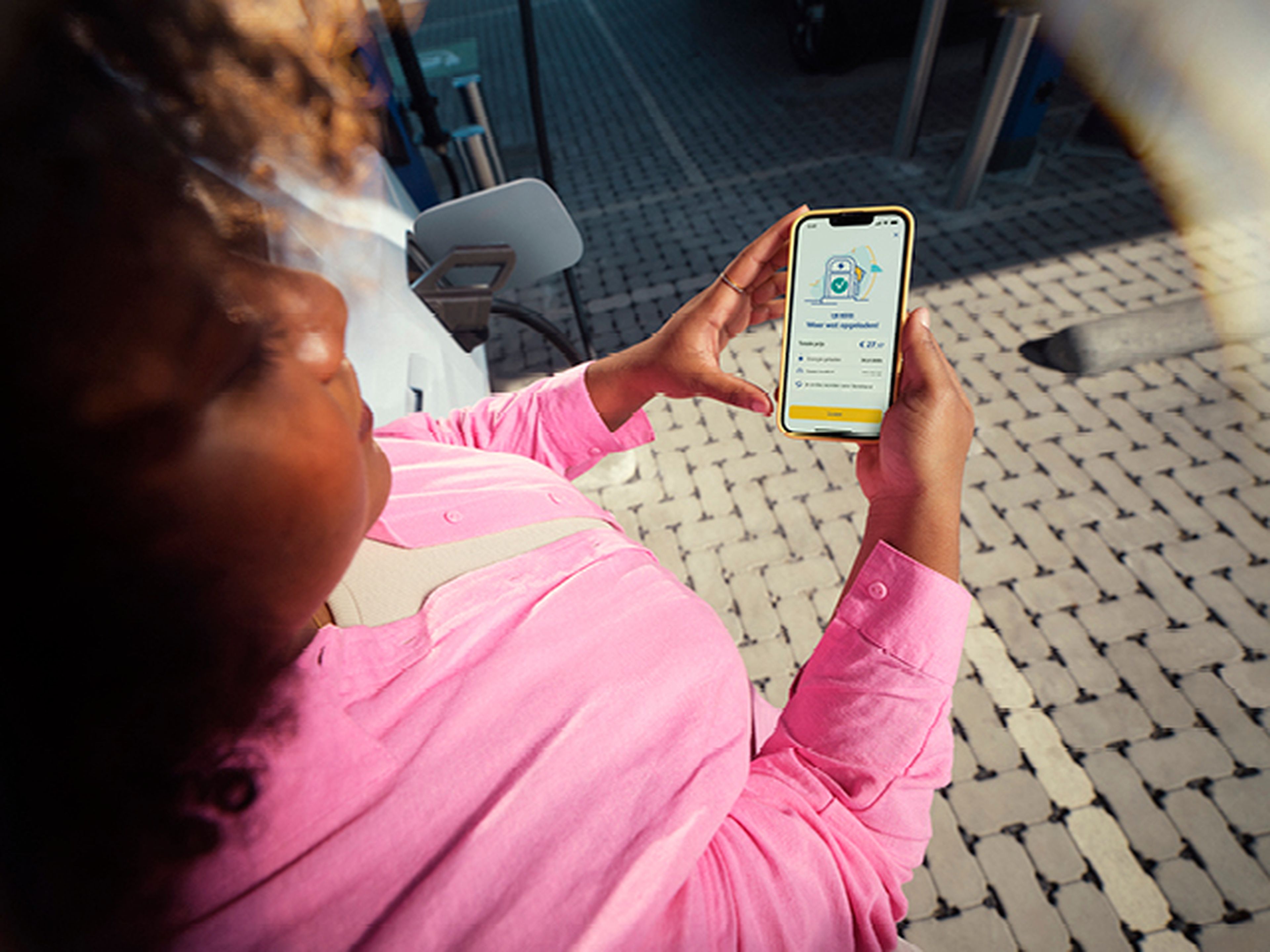 Woman looking at her phone with the Q8 electric app at a Q8 charging station.