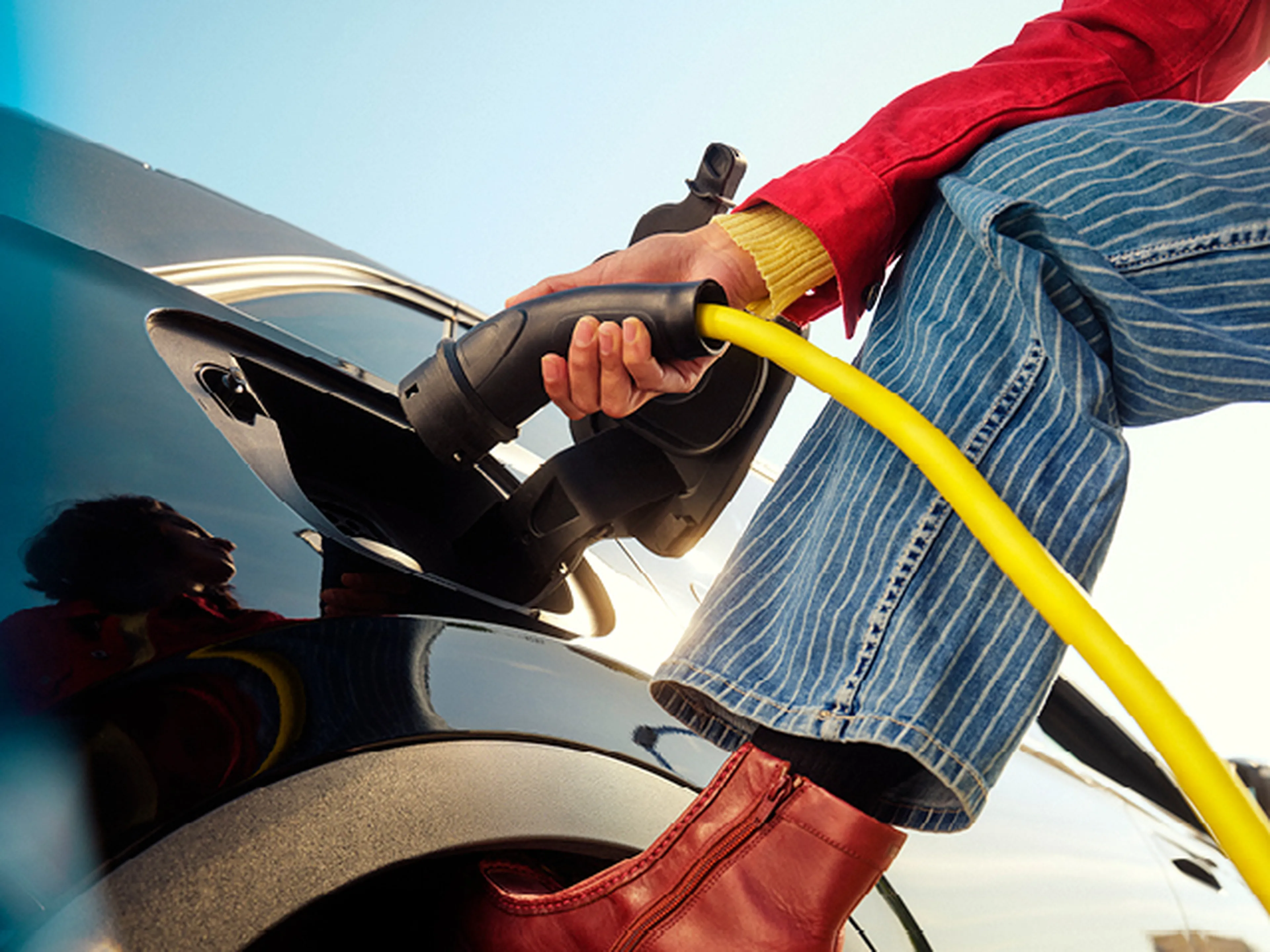 Close-up van een persoon die een gele laadkabel aansluit op een elektrische auto.