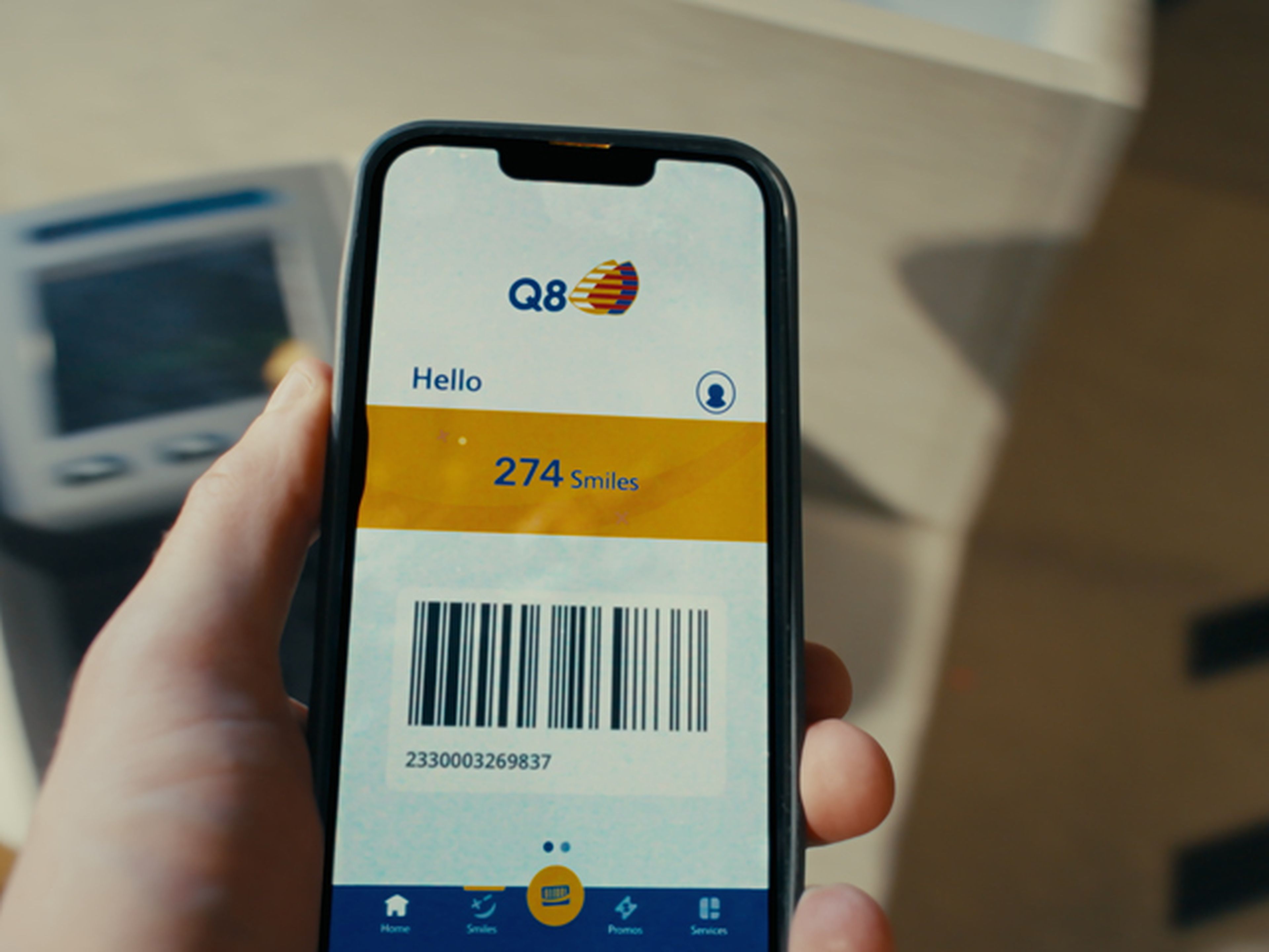 Appli Q8 sur un smartphone à coté d'un terminal bancaire chez Q8
