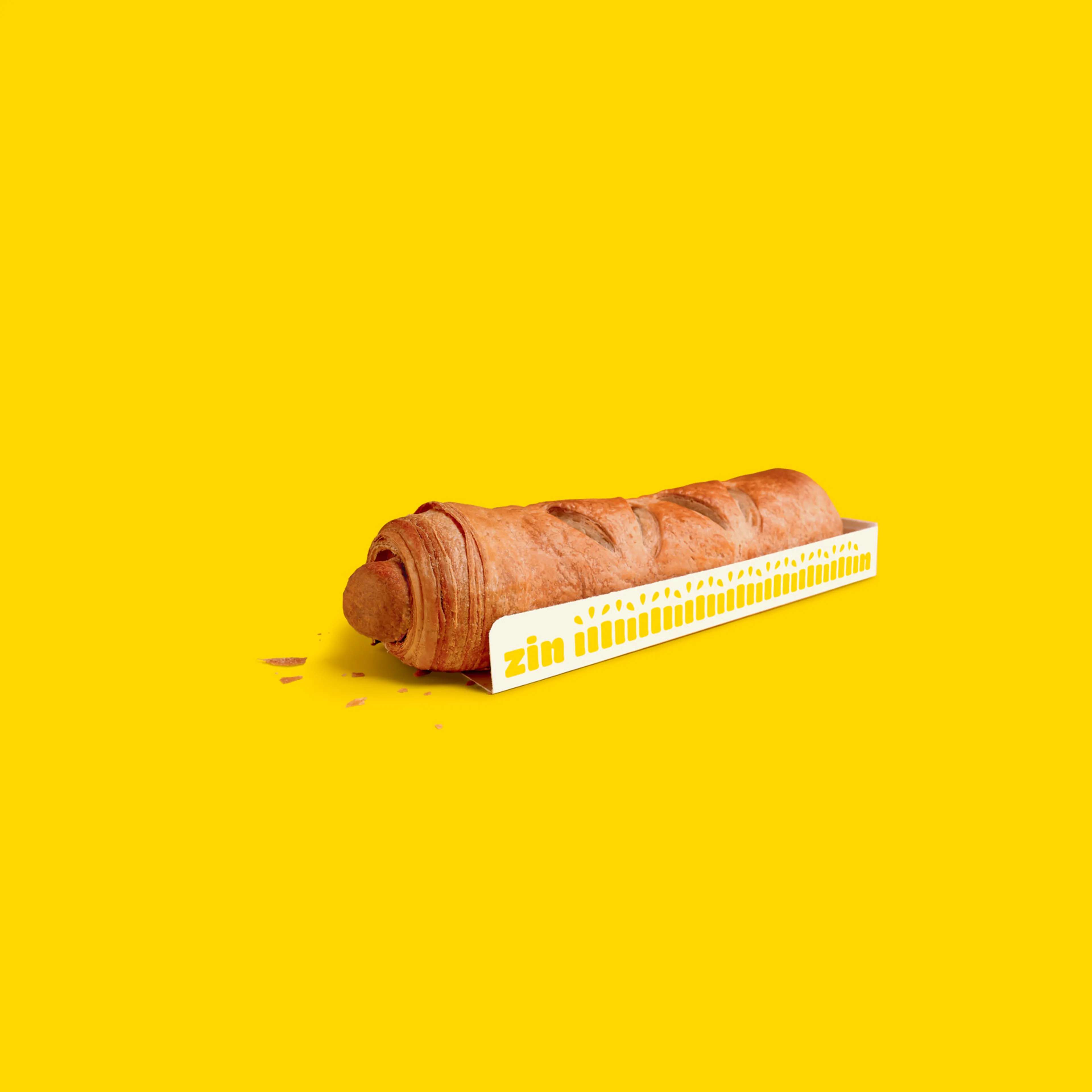 Vegetarisch worstenbroodje van Panos op felgele achtergrond, met kaartje waarop ‘zin in’ staat.