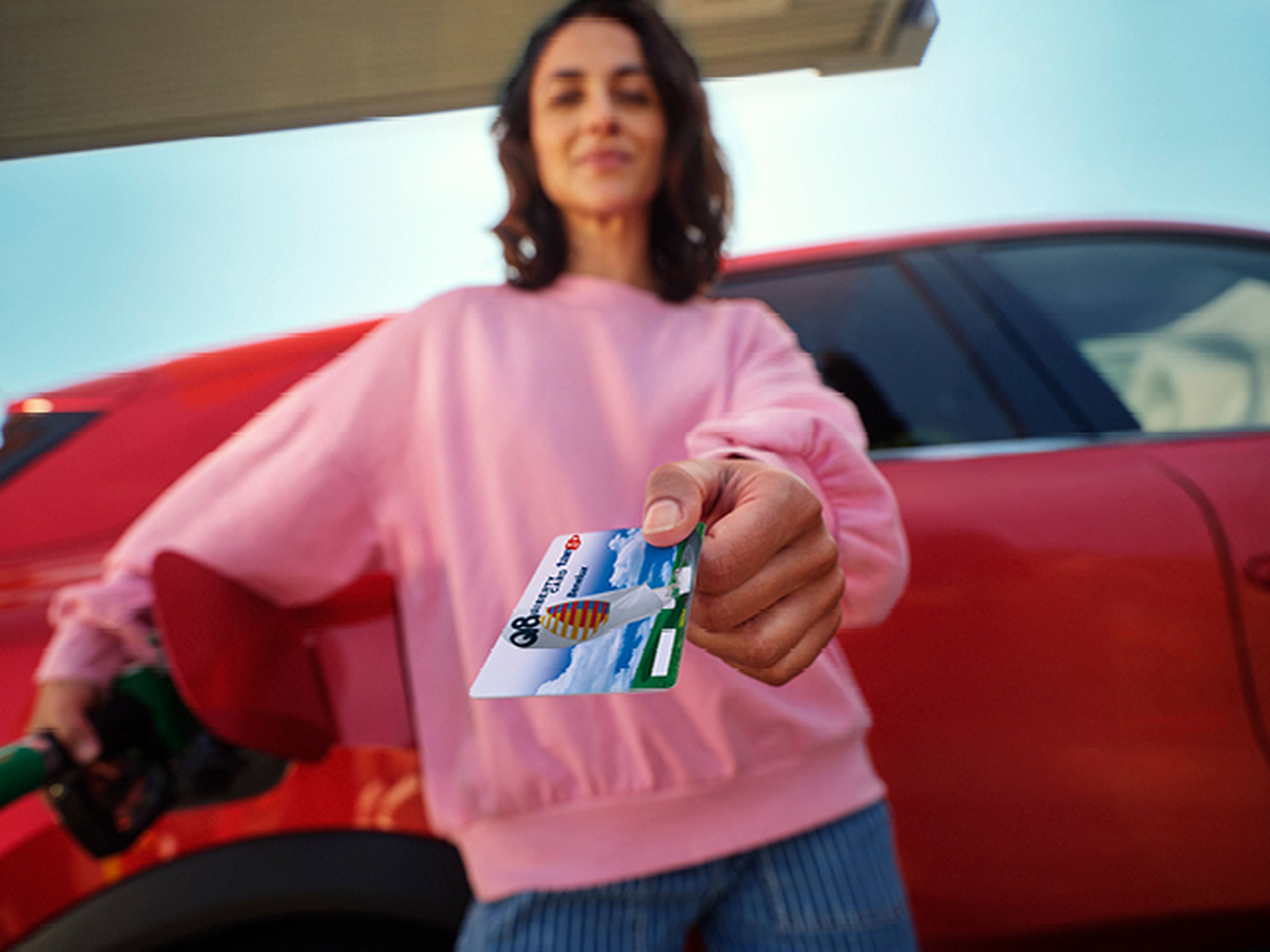Femme montrant une carte Q8 Liberty près de sa voiture rouge chez Q8.