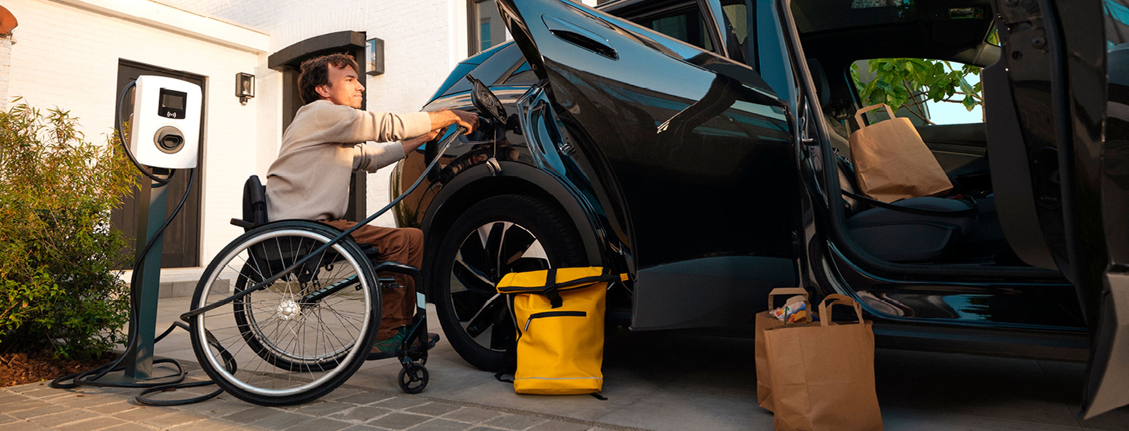 Man in rolstoel laadt elektrische auto op met een thuislader van Q8 electric.