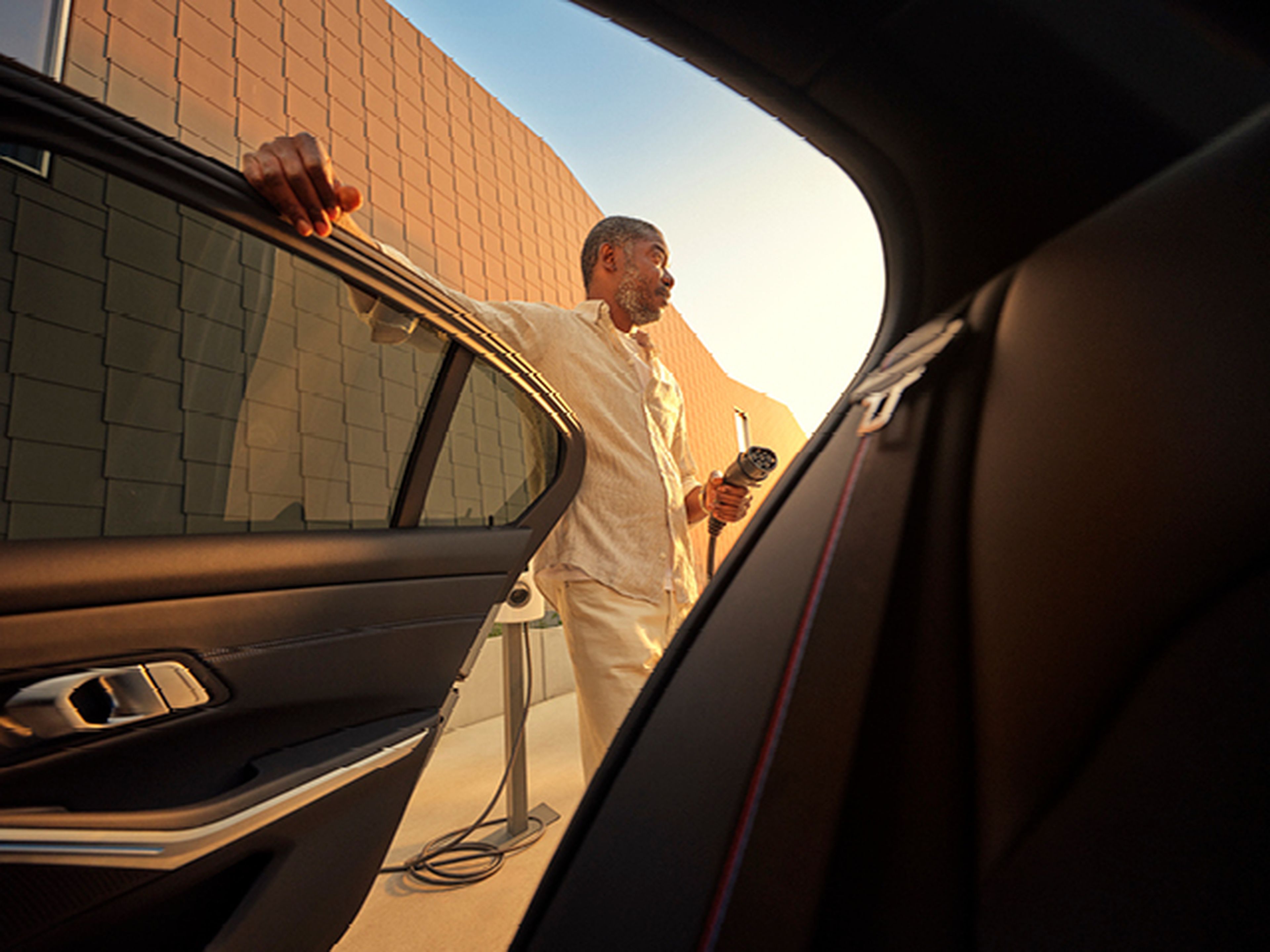 Man with charging cable near electric car, viewed from inside, at Q8.
