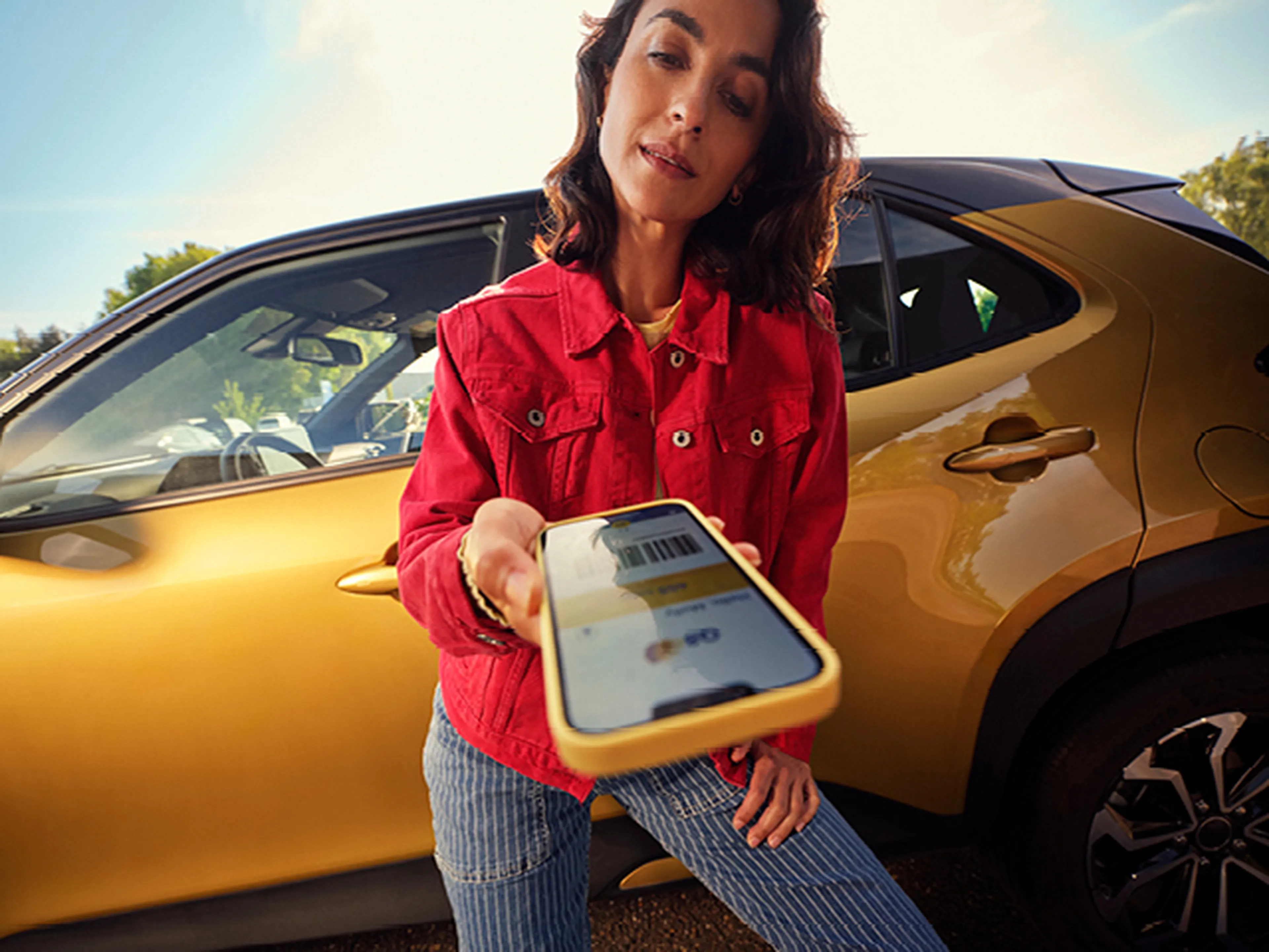 Femme présentant son smartphone devant son véhicule électrique lors d’une recharge Q8 electric.