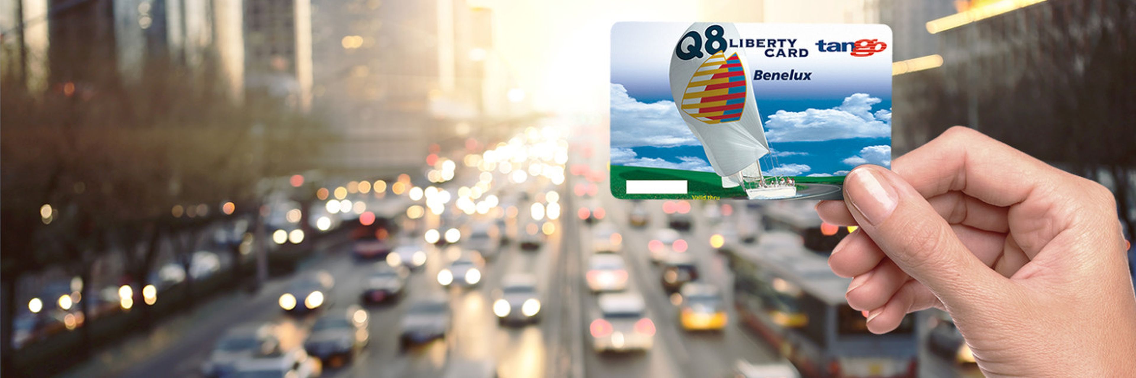 La carte Q8 Liberty est tenue, avec des voitures en arrière-plan.