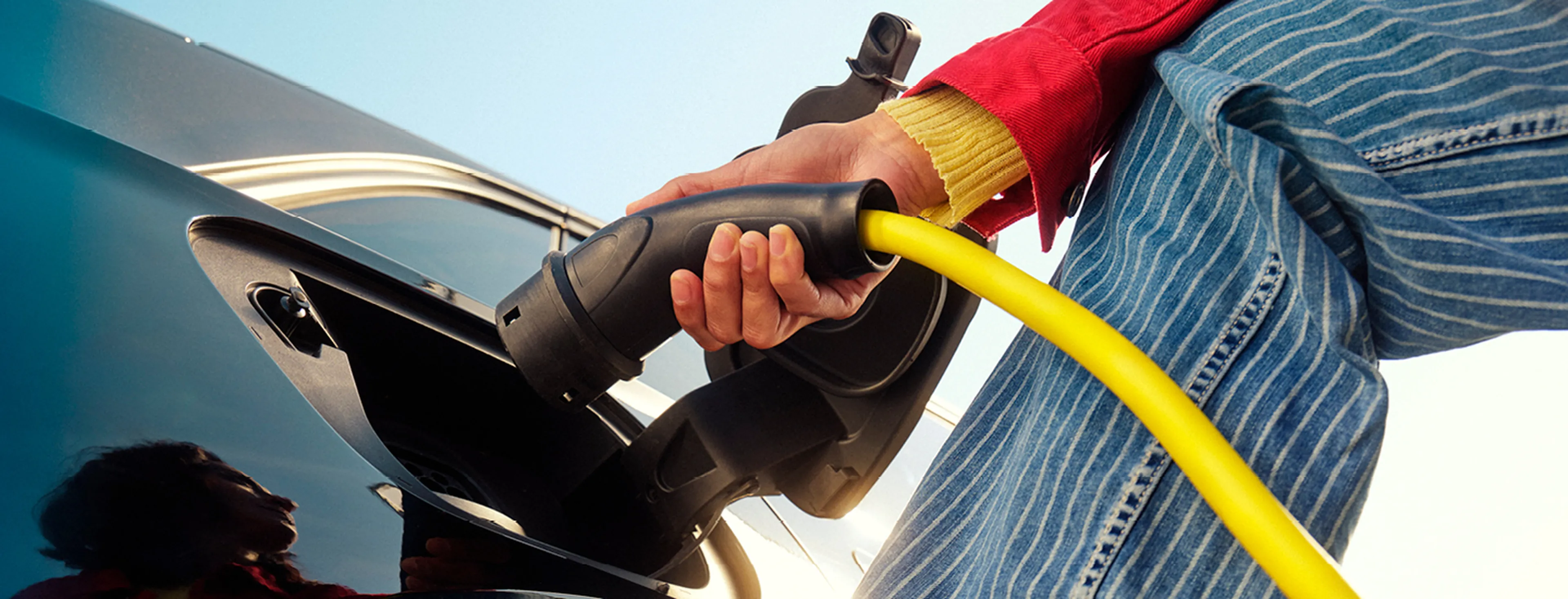 Close-up van een persoon die een gele laadkabel aansluit op een elektrische auto.