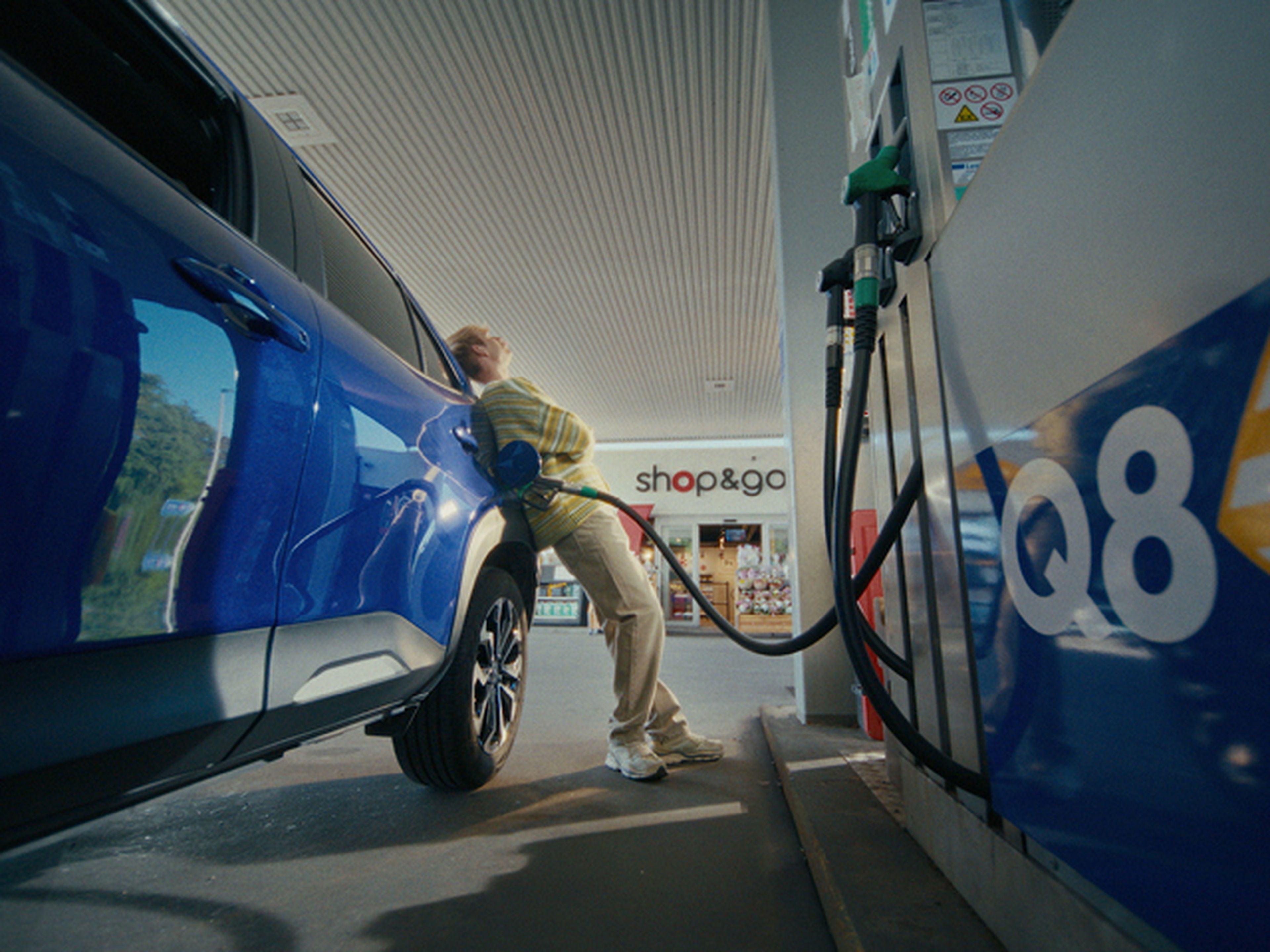 Man leans against car while refueling at Q8.