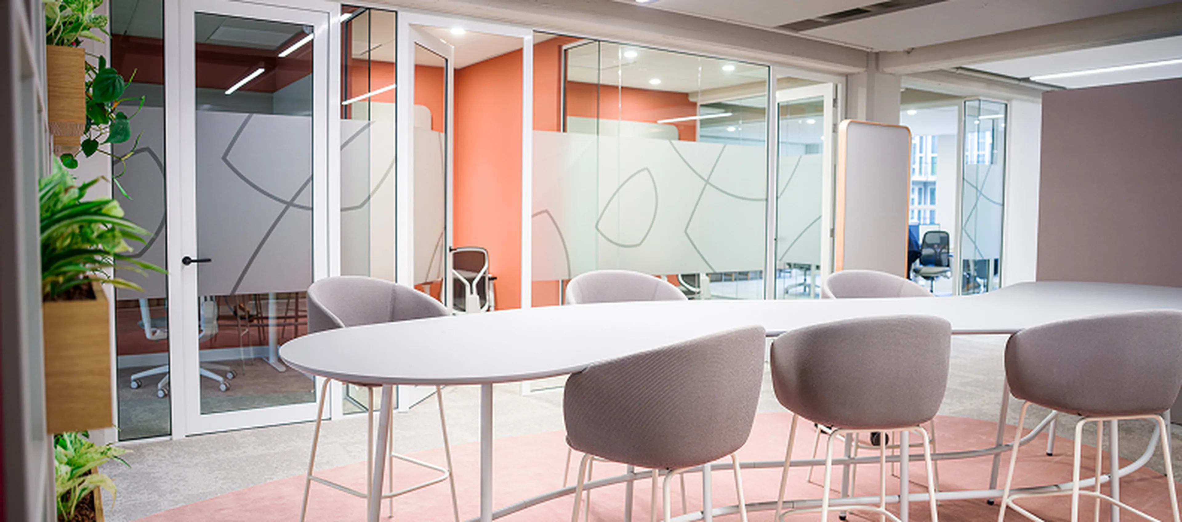 Meeting room at the Q8 headquarters in Rotterdam with round tables, high chairs, and lots of glass. Warm colors and plants create an open and fresh atmosphere.