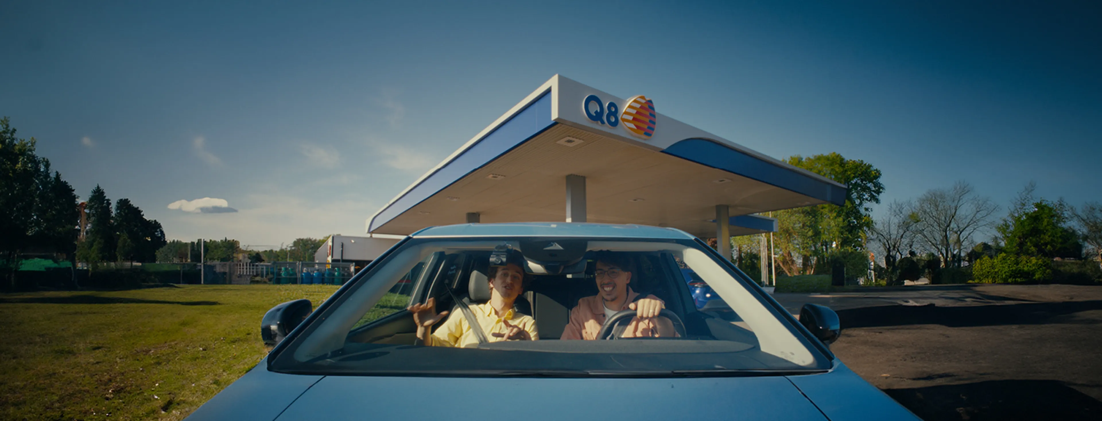 Twee mannen zitten in de auto en rijden weg van bij een Q8 station.