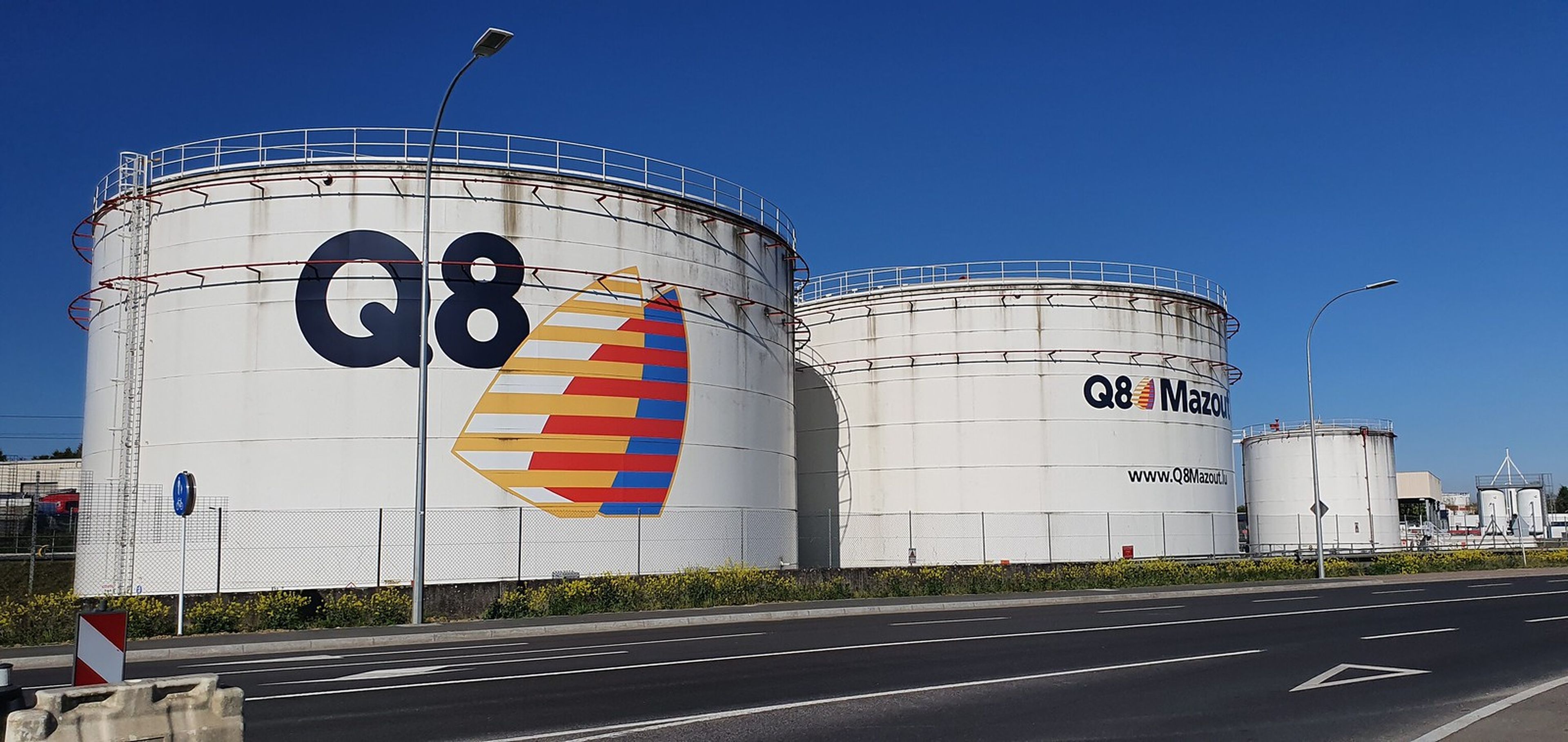 Trois grands réservoirs de stockage blancs de Q8 le long d’une route, avec le logo Q8 sur le réservoir de gauche.
