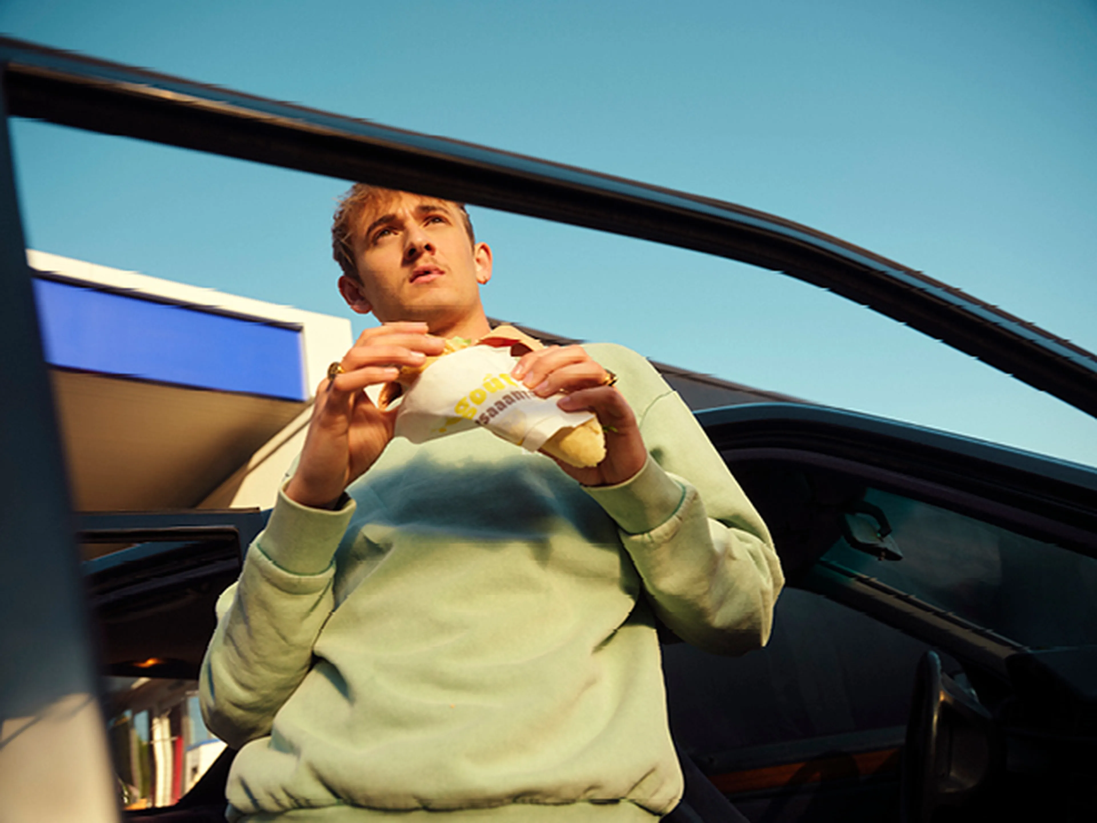 Man staat aan zijn auto met Panos broodje bij een Q8 station