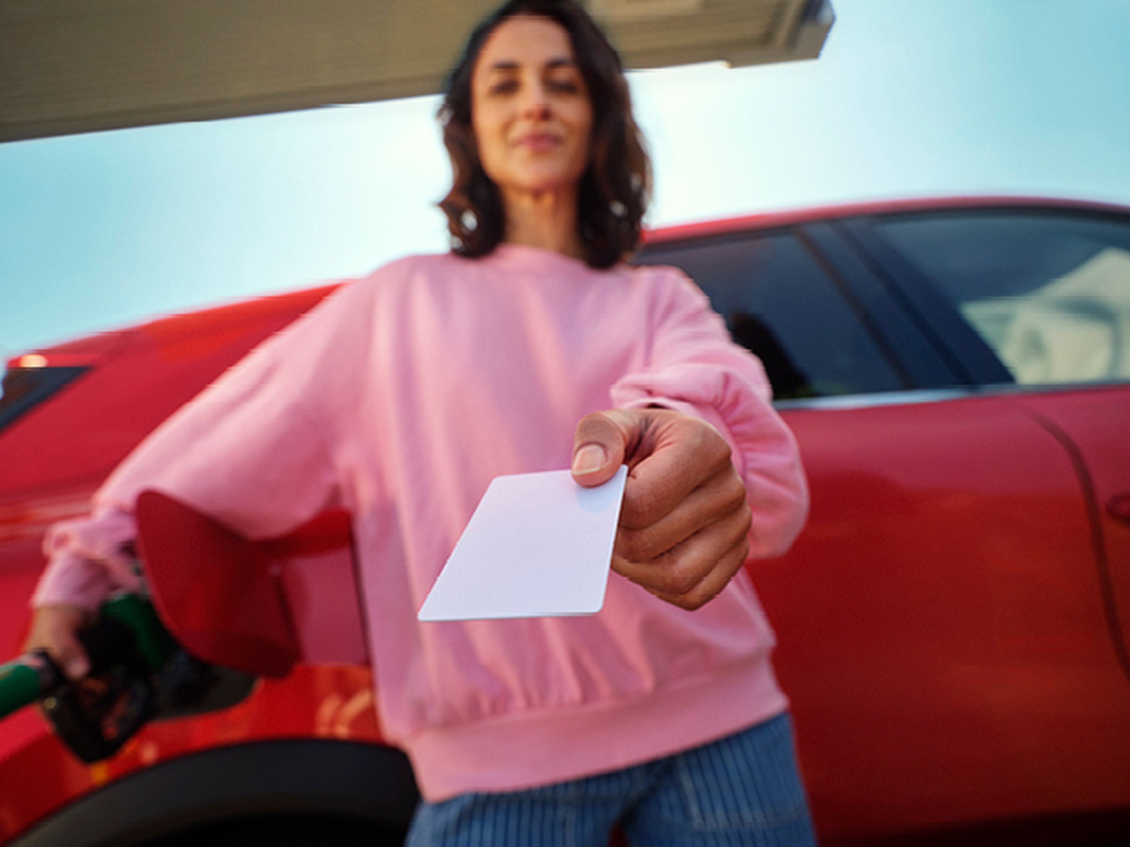 Femme montre une carte Q8 Liberty en faisant le plein d'une voiture rouge.