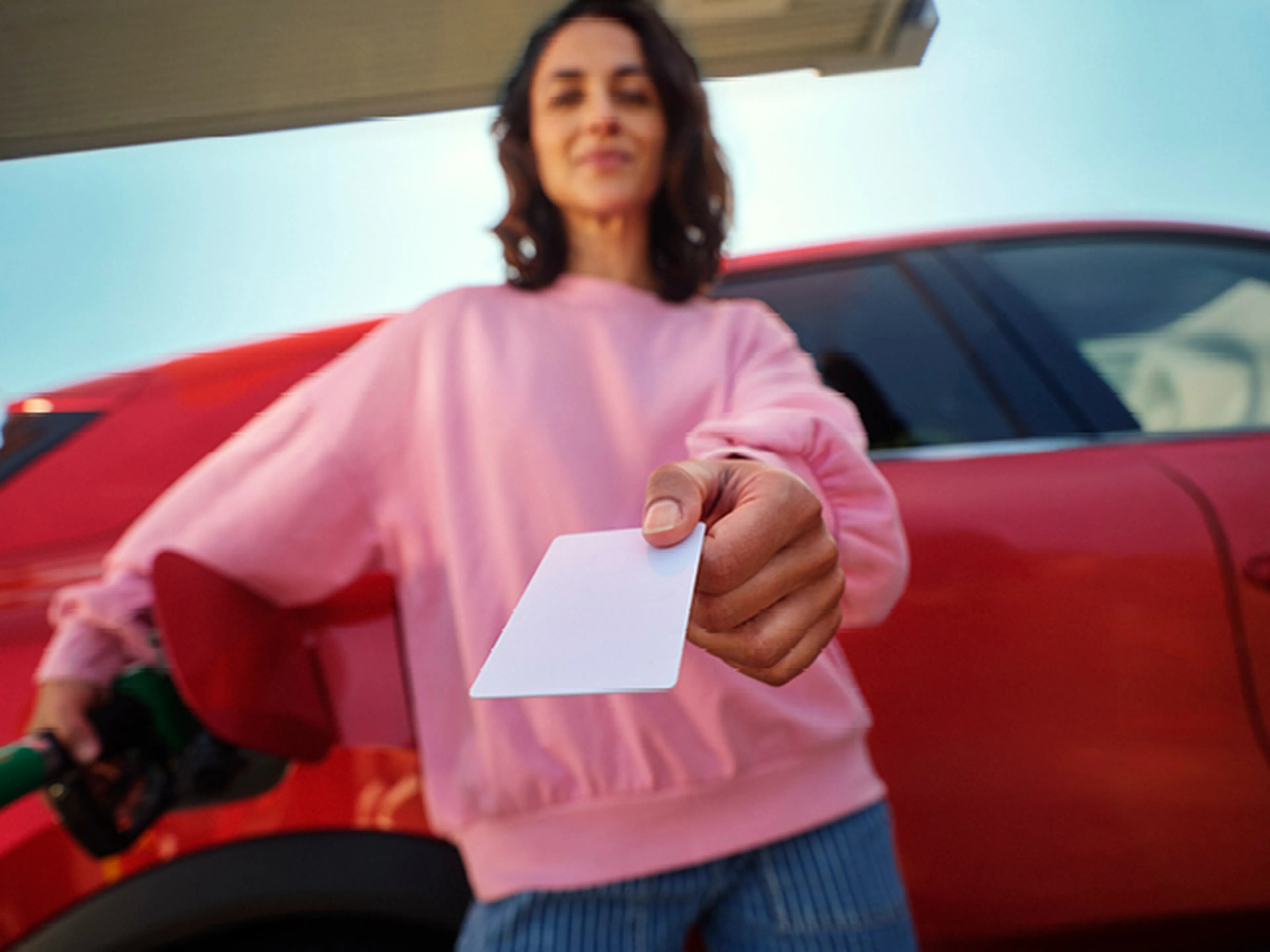 Woman showing a Q8 Liberty Card while refueling a red car.
