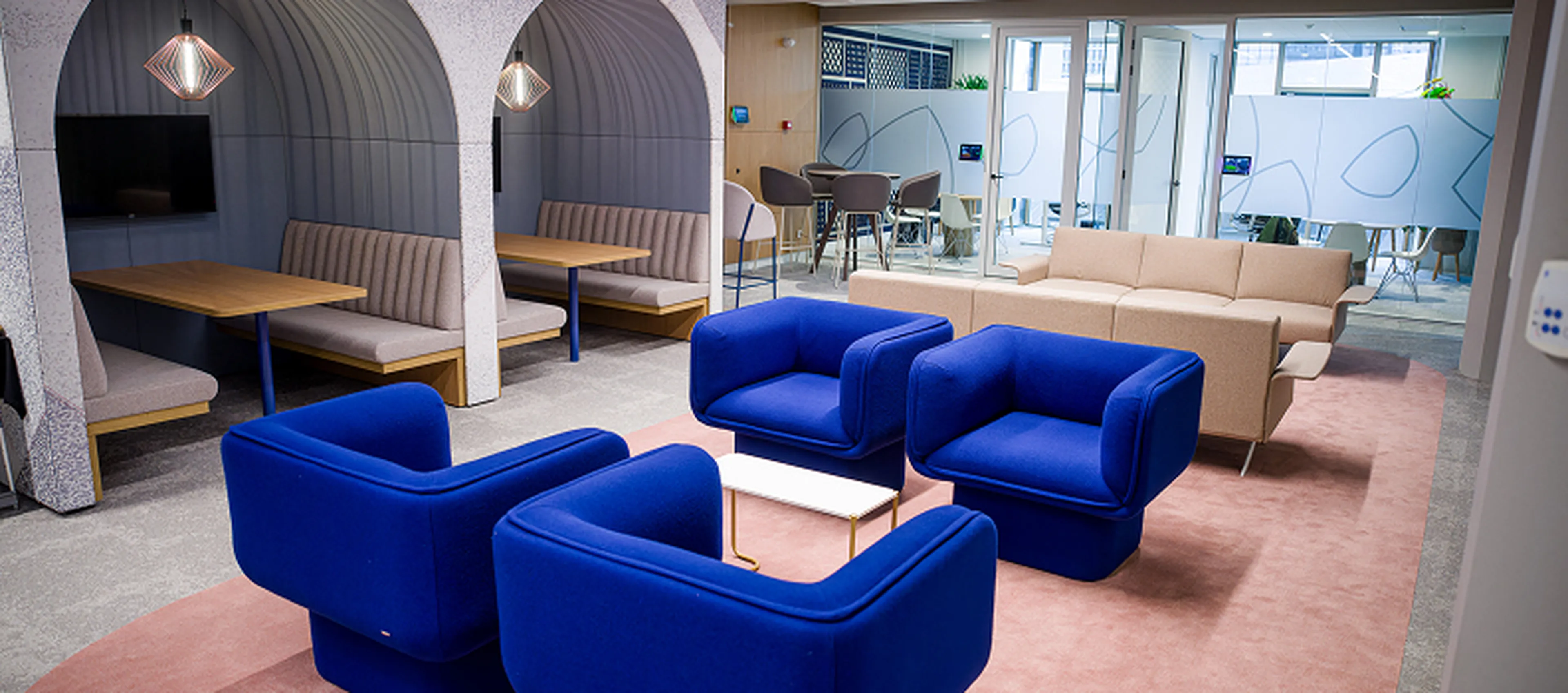 Lounge area at the Q8 headquarters in Rotterdam with bright blue armchairs, beige sofas, and covered seating alcoves with tables.
