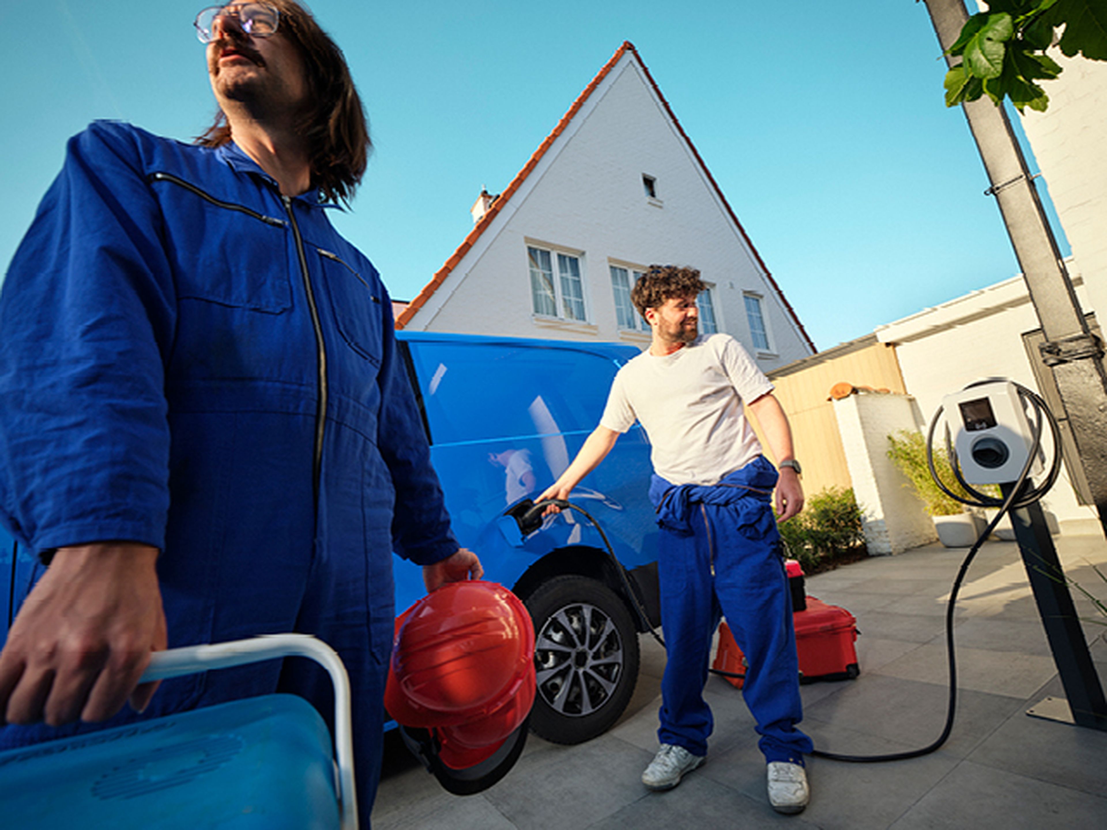Hommes rechargent une camionnette bleue avec une borne de recharge domestique Q8.