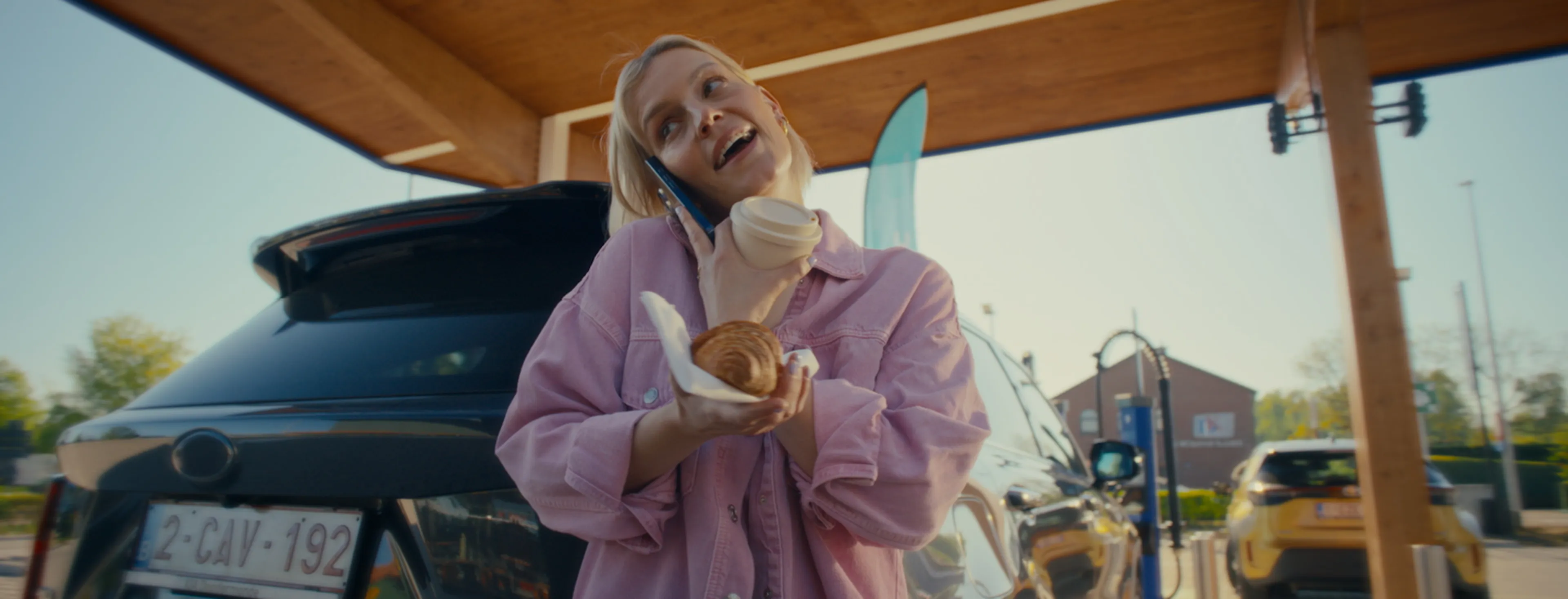 Woman charging her electric car while talking on her smartphone.